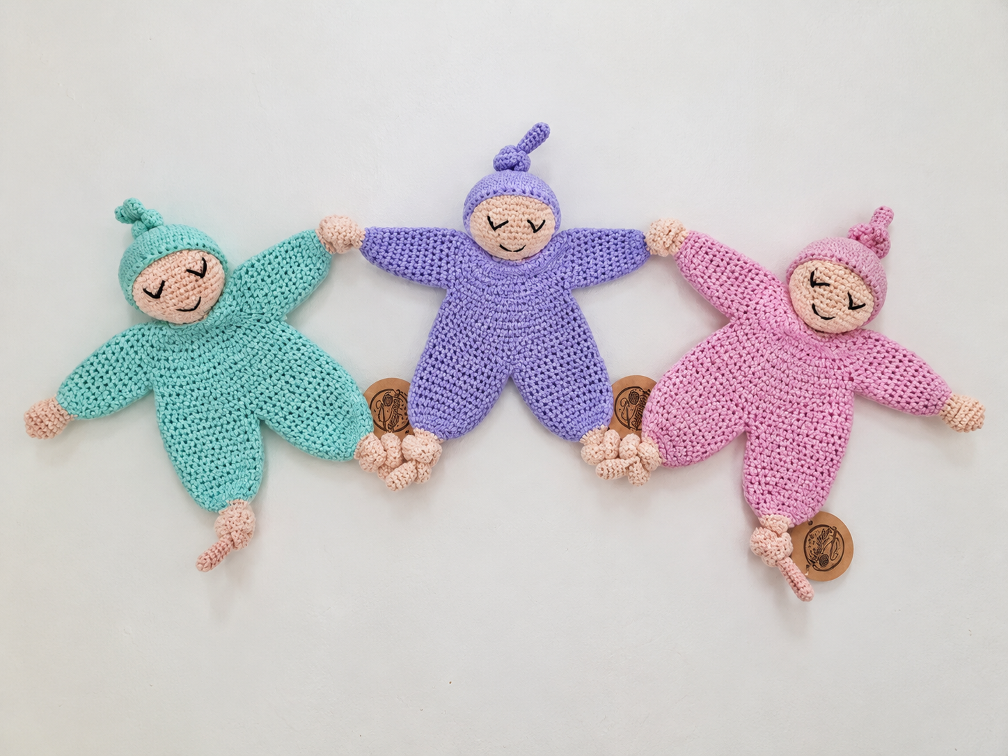 Drei gehäkelte Kuschelinos mit Zipfelmützen in Mint, Lavendel und Rosa